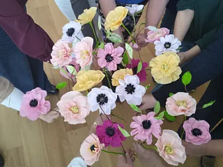 Hænder holder papirblomster i lyserøde og gule farver